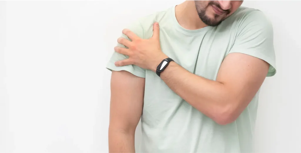 Oseba v svetli majici se drži za ramo zaradi bolečine