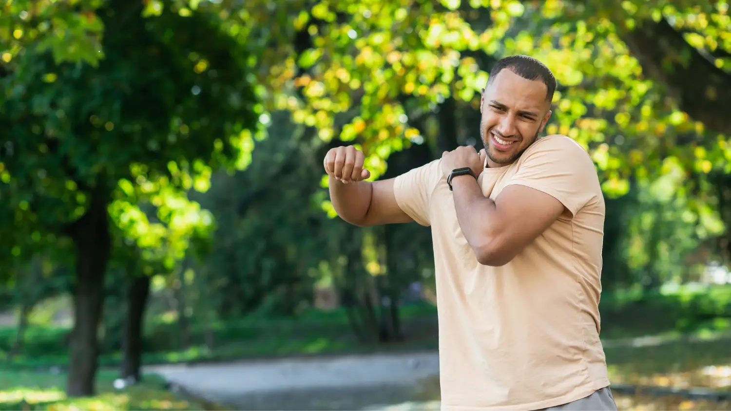 Bolečina v rami - Moški v bež majici se drži za ramo med hojo v parku